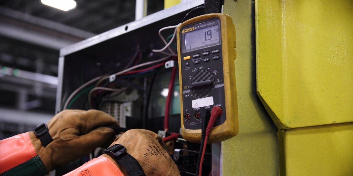 Électricien portant des gants isolants et mesurant avec un multimètre dans une armoire électrique